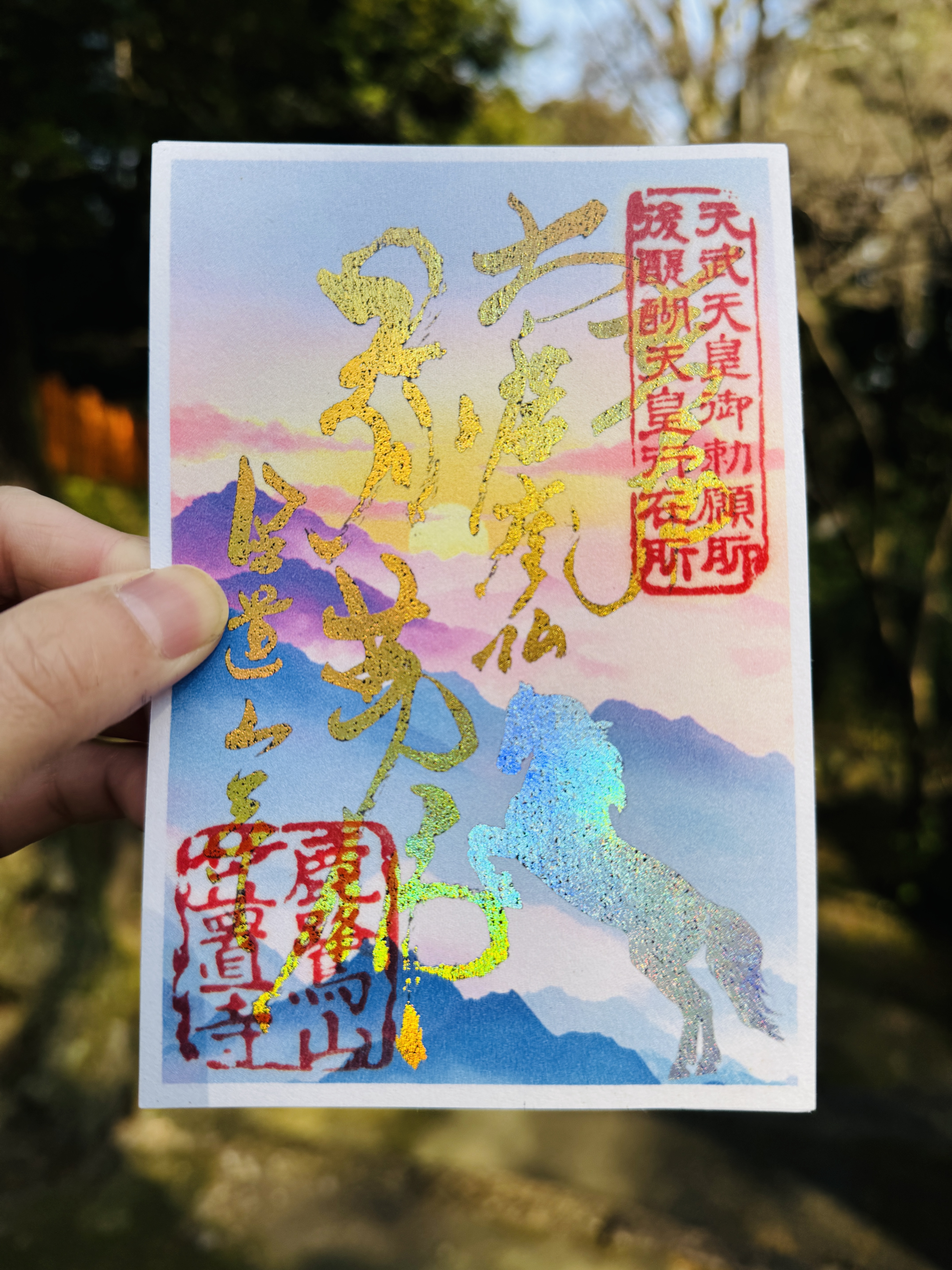 初日の出のグラデーション背景に、金色の箔押し文字とキラキラと輝く干支の馬がデザインされた御朱印。"